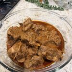 Slow-cooked meat with a rich gravy in a transparent glass platter