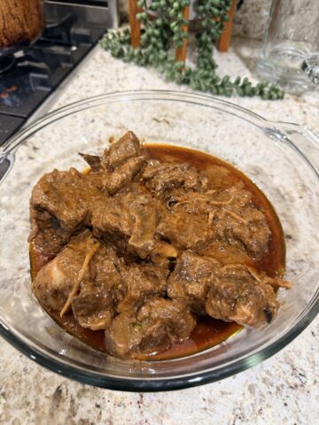 Slow-cooked meat with a rich gravy in a transparent glass platter